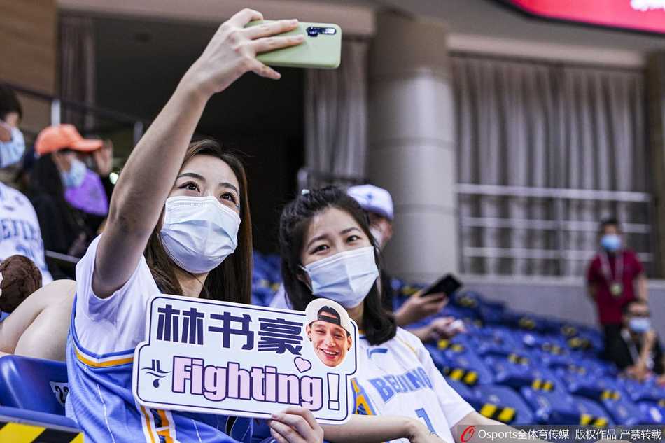 镜头聚焦在看台，一位美女粉丝面对镜头比出胜利手势，她身后是“林书豪美女粉丝团”的横幅，显示出粉丝团的组织有序。